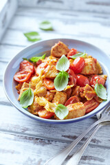 Farfalle pasta with chicken breast, cherry tomatoes and fresh basil. Bright wooden background.