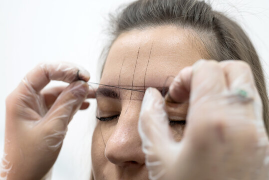 Permanent makeup, eyebrow tattoo. The master draws lines with a thread, makes a sketch of the eyebrows. Professional face care.
