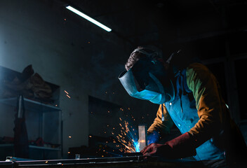 Craftsman welding metal profile while working in unlit workshop 