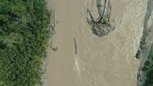 Top view, following a wooden canoe with a motor on the back driving over a large river in the amazon of South America

