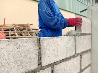 Worker installing cement blocks wall with mortar in construction site closeup.