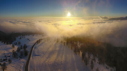 Aerial drone flight between clouds during winter season. A pale sun shines above the clouds after a...