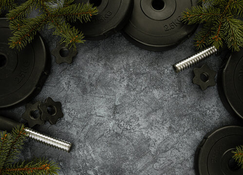 Heavy Dumbbells Weight Plates And Christmas Tree Branches. Healthy Lifestyle Holiday Season Composition. Festive Flat Lay Concept With Copyspace. Exercise In Cold Winter Weather.