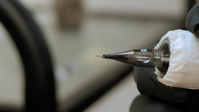 Close-up of a tattoo machine with a single needle and black ink, the machine is turned on and the needle is moving. The process of tattooing on the skin.