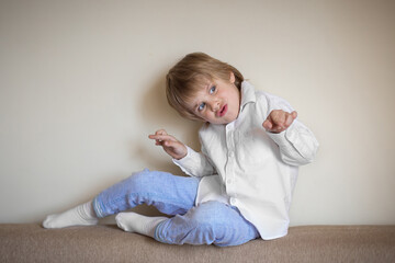 Fototapeta premium A five-year-old boy in a white shirt and blue pants is sitting in a beige room