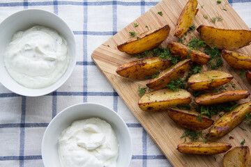 Potato wedges with dip, oven roasted, with dip and dill, on a kitchen board, on the tablecloth, top view