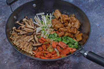 Vegan stir fry in black wok on gray background, copy space