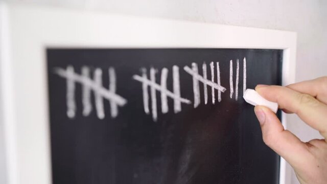 Man's hand with a chalk making a vertical bar line on the chalkboard surface counting a days or exercises sets. Time going or counting process concept 4K footage.