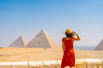 A young tourist in a red dress looking at the Pyramids of Giza, the oldest Funerary monument in the...