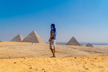 Portrait of a young man in a blue turban walking next to the Pyramids of Giza, the oldest Funerary...