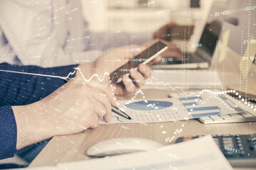 Double exposure of man's hands holding and using a digital device and forex graph drawing. Financial market concept.