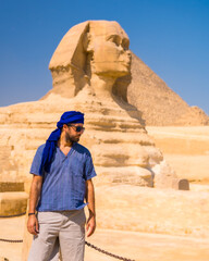 Fototapeta na wymiar A young tourist near the Great Sphinx of Giza dressed in blue and a blue turban, from where the miramides of Giza, cultural tourism and a lot of history. Cairo, Egypt