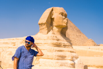 Fototapeta na wymiar A young tourist at the Great Sphinx of Giza dressed in blue and a blue turban, from where the miramides of Giza. Cairo, Egypt