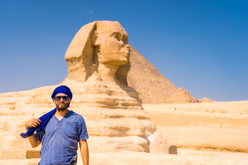 Fototapeta na wymiar A young tourist at the Great Sphinx of Giza dressed in blue and a blue turban, from where the miramides of Giza. Cairo, Egypt