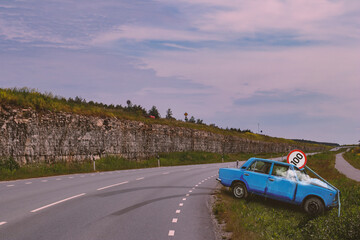 A blue vintage Lada 21011 car having lost control in a highway curve by a mountain cliff and crashed against a speed limit traffic sign