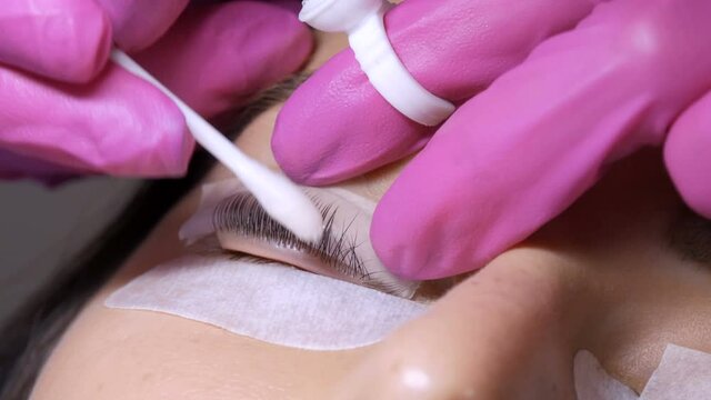 Face of a young girl before a modern eyelash lamination procedure in a professional beauty salon. The master washes off the special glue with a cotton swab before the eyelash curling procedure.