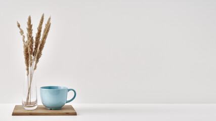 A vase with dry spikelets and a mug stand on a wooden stand on a white background. Minimalism, eco-materials in the interior decor. Copy space, mock up.