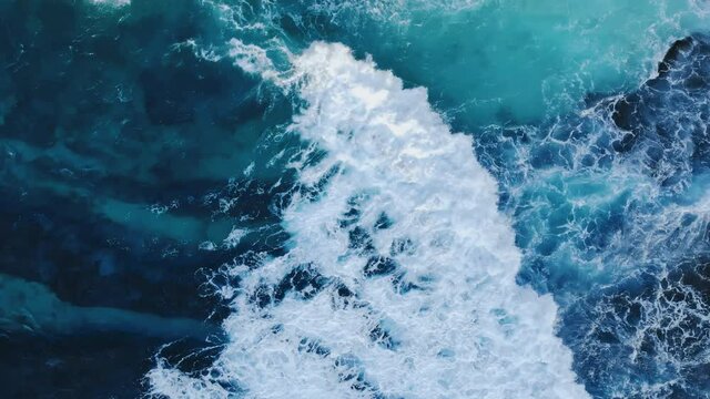 Top down relaxing view of azure water waves meeting with rock cliff. Beautiful scene of sea tides power, rising seafoam. Tropical landscape of amazing colourful untouched nature. Concept of travel.