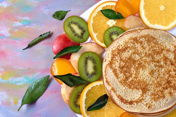 pancakes with persimmon apples and kiwi on a white plate on a variegated table
