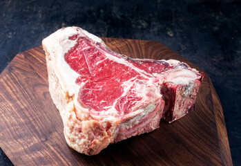 Raw dry aged wagyu t-bone beef steak offered as close-up on modern design wooden board