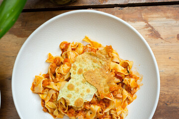 Pappardelle pasta with meat sauce on white ceramic plate in the table