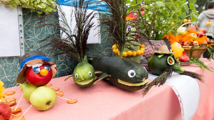 Animal figurines and fairy-tale characters made from fruits and vegetables lie on a table at the village fair in honor of the harvest.