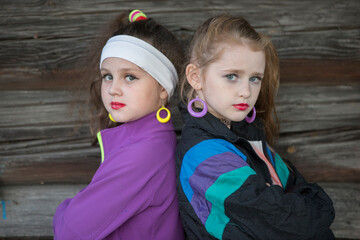 Little girls in bright clothes with makeup on their faces on a wooden background. A child in the style of the nineties.