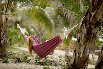 travel photo of the red girl in hat lying on the hammock on tropical beach with hammock