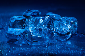 Melting frozen ice cubes illuminated with blue coloured LED light in the dark.