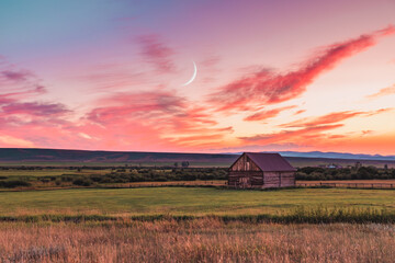 A beautiful sunset in a rural Montana scene. A simple barn sits in a field as the sun sets while...