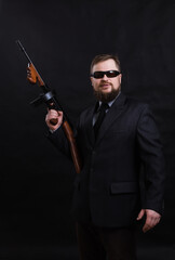 Mature bearded man in sunglasses dressed in suit with tommy gun