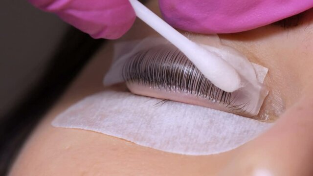Face of a young girl before a modern eyelash lamination procedure in a professional beauty salon. The master applies special glue before the eyelash curling procedure in pink rubber gloves close up.