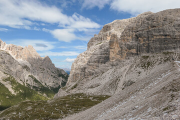 Panoramic view on a valley in Dolomites, Italy. There are sharp and steep mountain slopes around. Lots of lose stones and pebbles. The sky is full of soft clouds. Raw landscape. Serenity and calmness