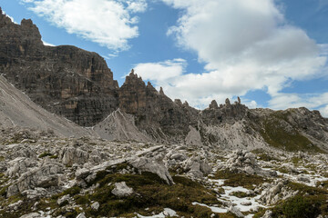 Obraz premium A close up view on high and sharp peaks of Dolomites in Italy. The sky is full of soft clouds. Lots of lose stones and pebbles. Raw and desolated landscape. Serenity and calmness