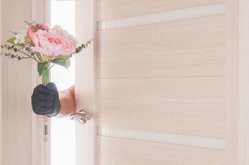 Hand in medical glove gives bouquet of flowers through the doorway