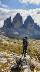 A man in hiking outfit enjoying the view on the famous Tre Cime di Lavaredo (Drei Zinnen), mountains in Italian Dolomites. Desolated and raw landscape, full of lose stones. Overcast. Achievement