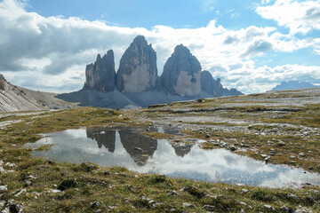 A panoramic view on the famous Tre Cime di Lavaredo (Drei Zinnen), mountains in Italian Dolomites. The mountains are reflecting in small paddle. Desolated and raw landscape. Natural phenomenon