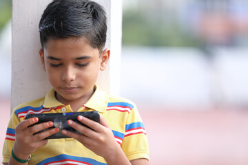 Portrait of Indian little boy playing game using mobile phone at home terrace	
