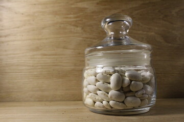 Fototapeta na wymiar white beans in a glass jar with a lid on a bright wood background there is a copy of the spays