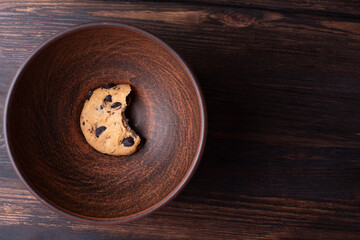 One bitten cookie in a plate on a dark wooden background, close up.