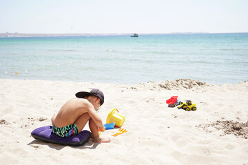 Fototapeta na wymiar boy dressed in a baseball cap playing on a sandy beach against a beautiful sea and sky background.
