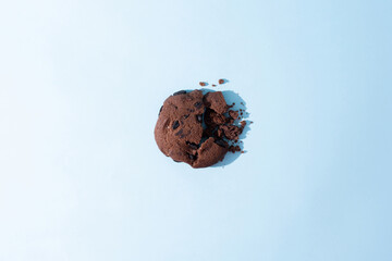 One broken chocolate chip cookie on blue background in sunlight.