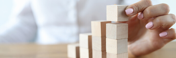Woman build tower from wooden cubes on table close-up. Career growth up stairs. Female hand put cube one by one.