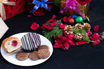 Sweet Dessert Chocolate Lollypop Slice Of Strawberry Croissant And Cookies Served In White Plate With Christmas Decoration Ornaments And Packed Gift Boxes Around On Dark Black Background