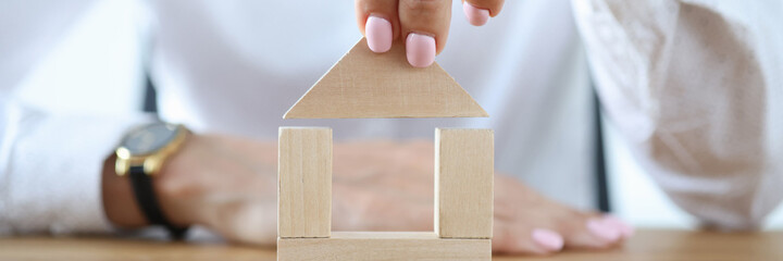Woman build house from wooden cubes on table. Purchase and construction of residential building.