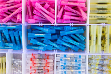 flat lay of solder seal butt connectors kit arranged in plastic box. Colored crimping equipment for permanent electric cable joining.