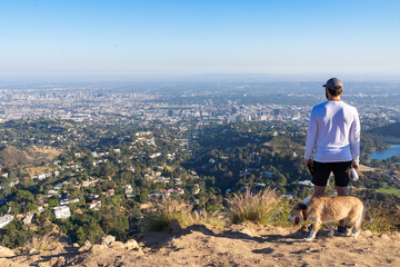 man hiking with his dog stops at the top of a mountain to overlook hollywood and greater los angeles
