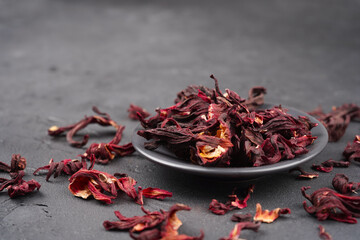 Fototapeta premium Hibiscus tea dried flowers in round plate on gray concrete background. Vitamin, recipe, beverage concept. Close-up, copy space