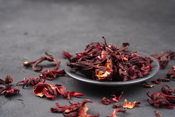 Hibiscus tea dried flowers in round plate on gray concrete background. Vitamin, recipe, beverage concept. Close-up, copy space