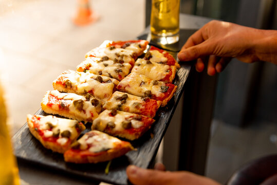 italian bruschetta close up during aperitivo. italian bread with tomato sauce and mozzarella with ham with natural light indoor in a bar, with hands serving it on table